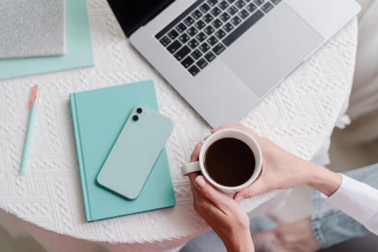 Woman holding a coffee mug at her desk with a laptop and an iPhone