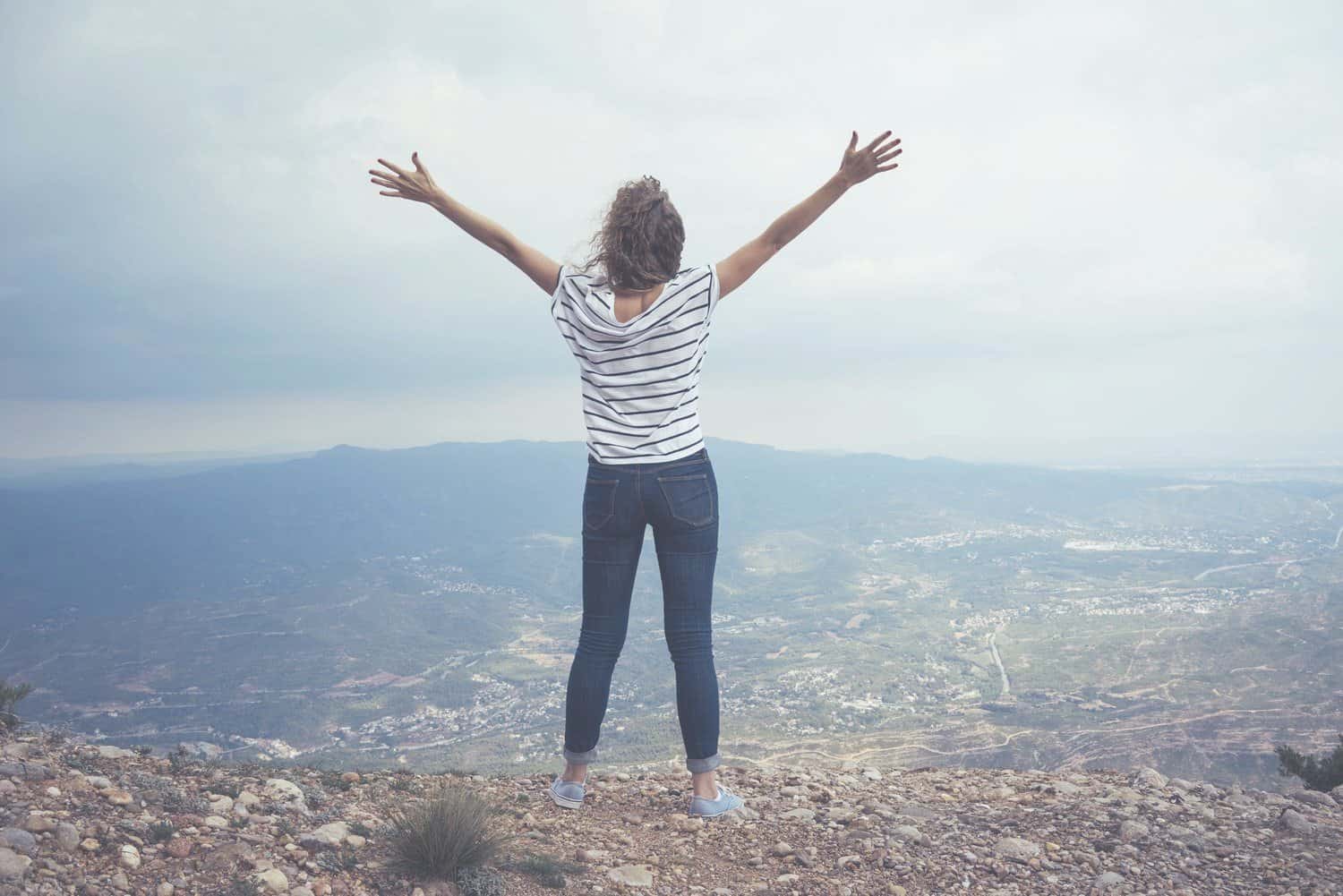 Powerful woman standing on the top of a mountain arms wide open