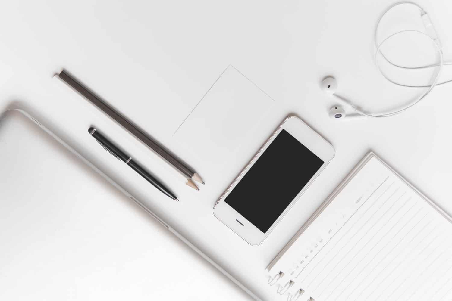 White productive office flat lay with a mobile phone, pens and a notebook