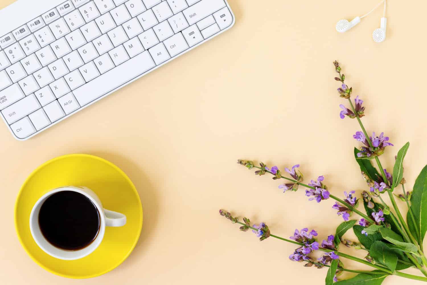 Top view of a productive home office desk with laptop, notebook, headphones, garden sage and coffee on yellow paper background. Flat lay, top view, copy space concept.