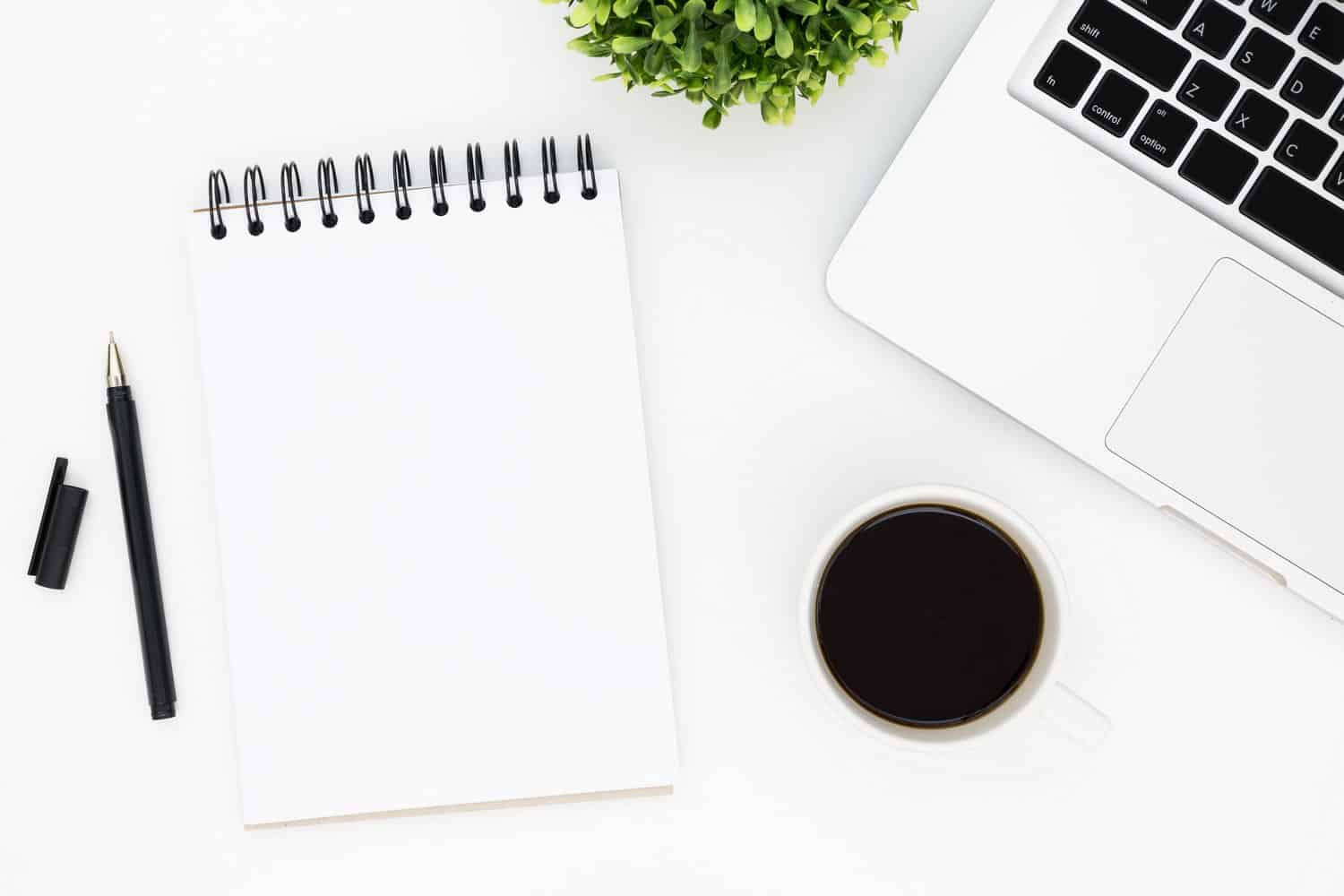 Productive flat lay with a laptop, notebook and a cup of coffee on a white desk