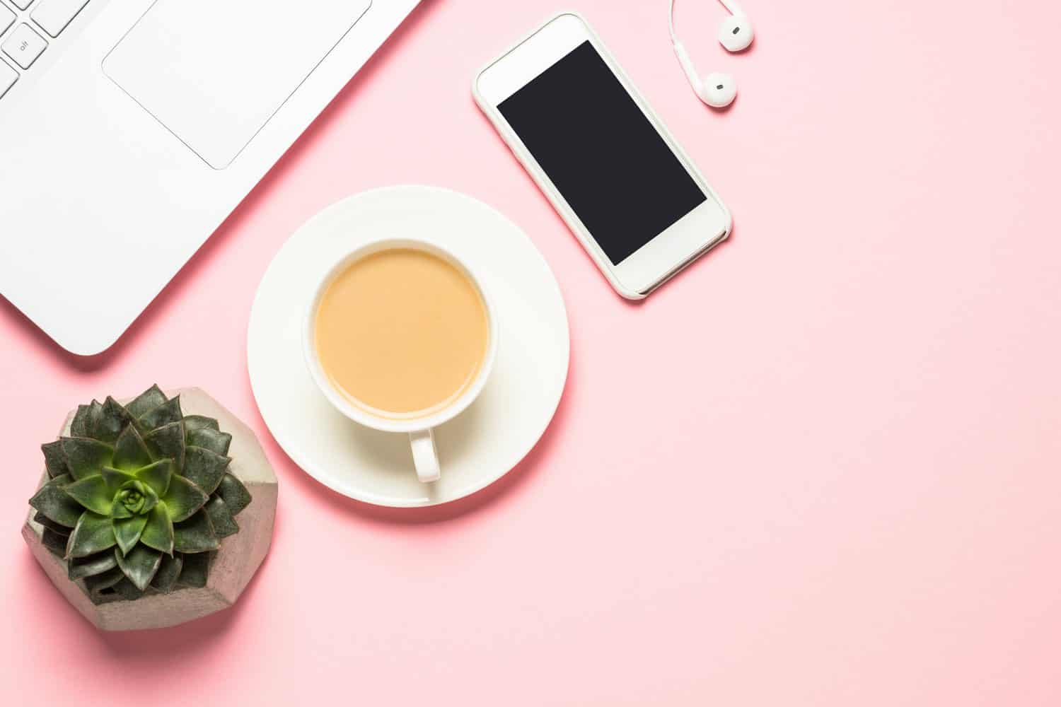 Laptop, phone, tea cup and a succulent on a pink background