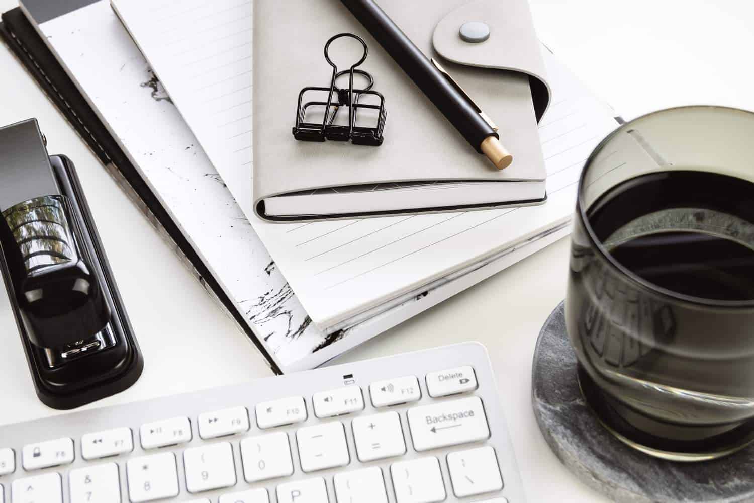 Coffee, white eyboard, gray notebook and a pen on a desk