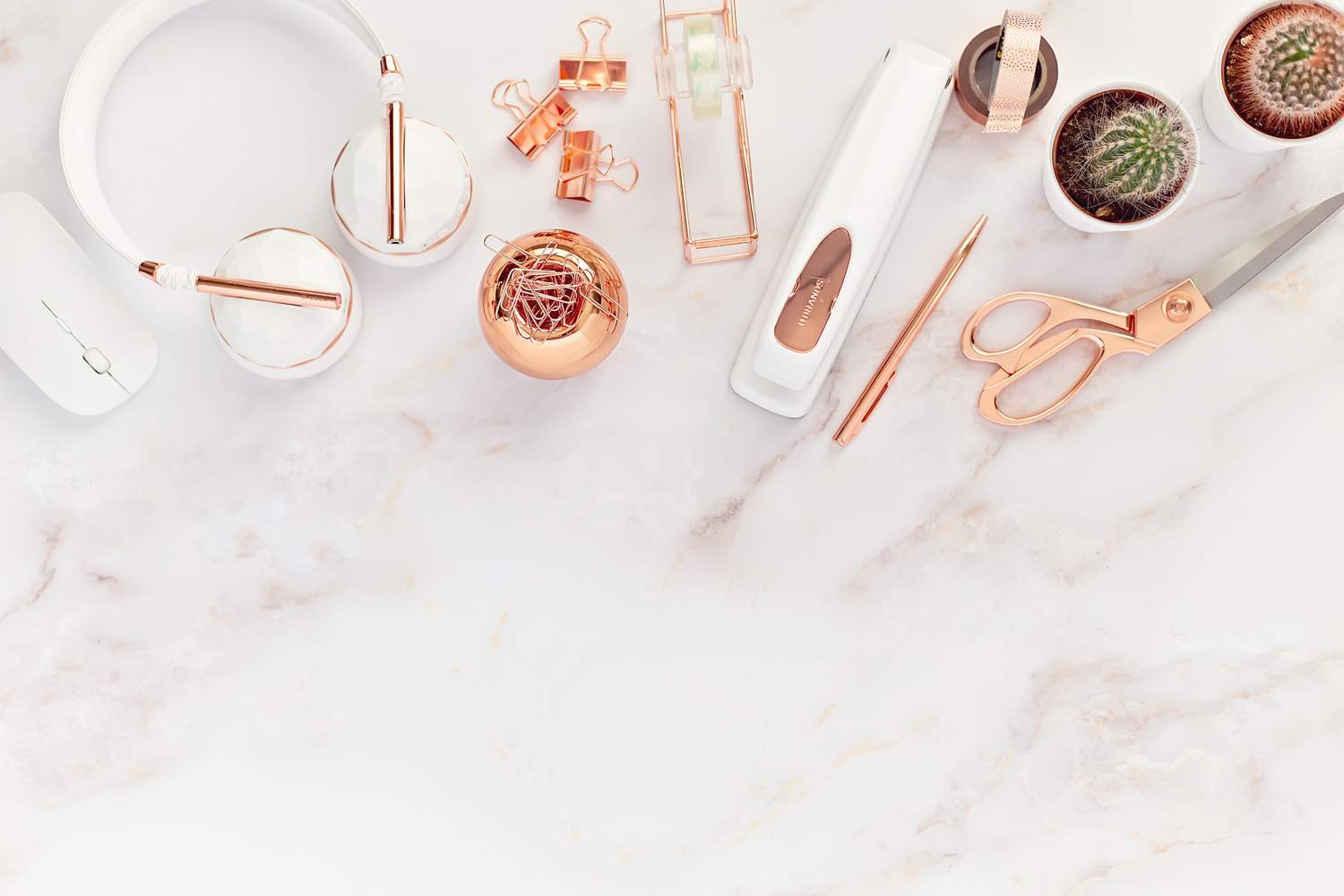White headphones, cacti, scissors and a stapler on a marble desk