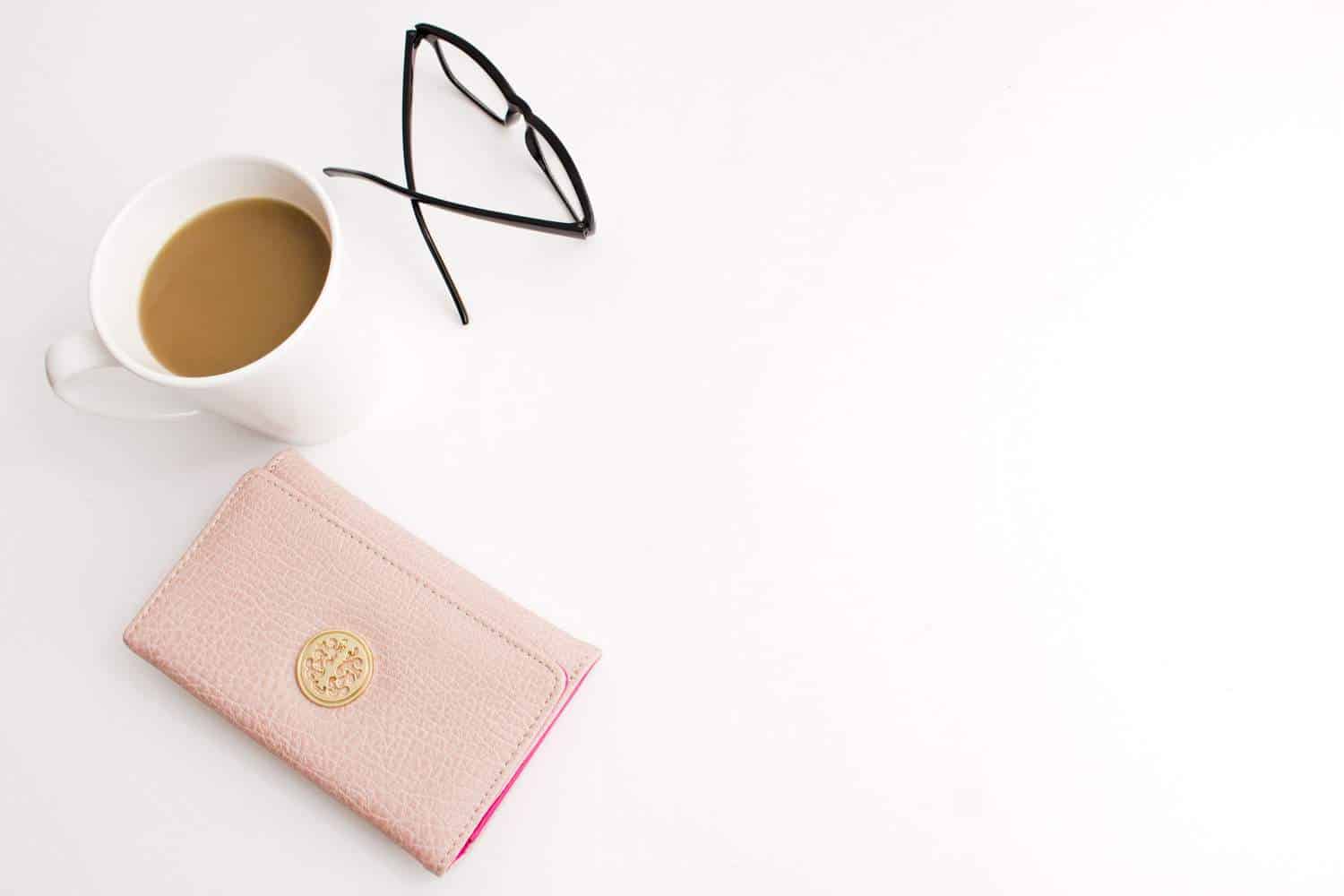 A morning coffee, pink wallet and glasses on a white desk