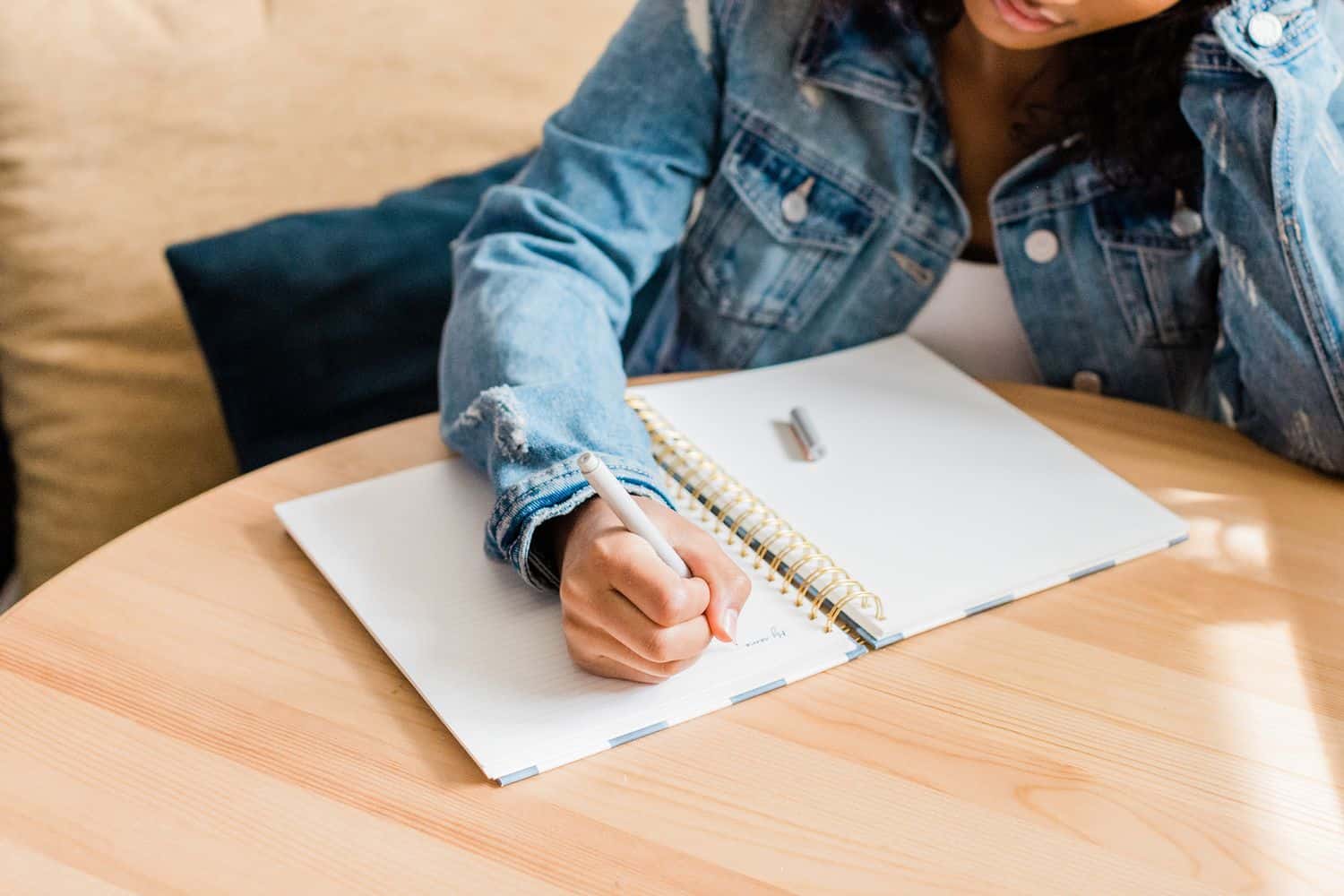 A woman sitting at a table writing on her notebook and leaning on her hand