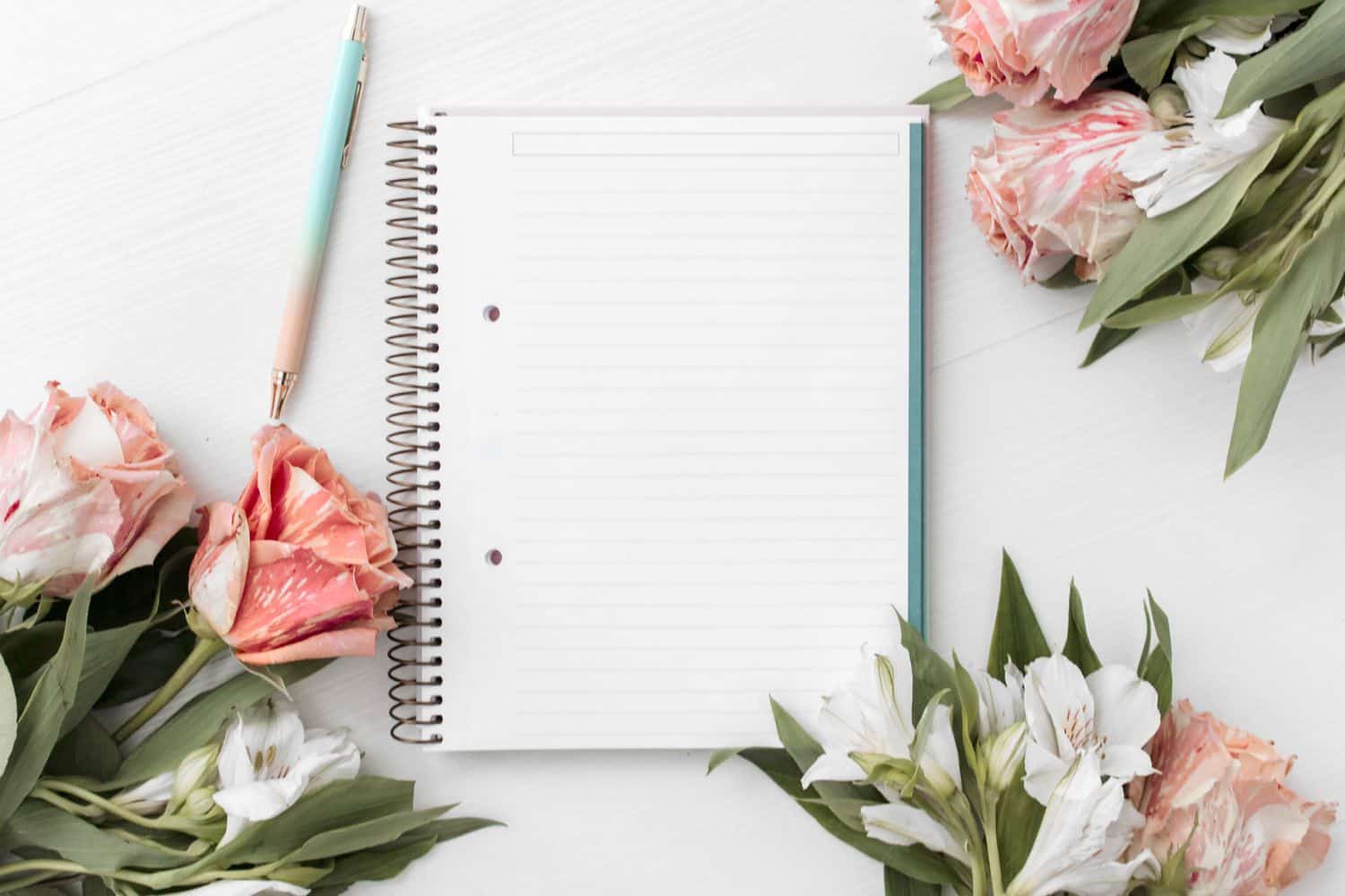 An empty notebook for affirmations, a pen and red and white flowers on a desk