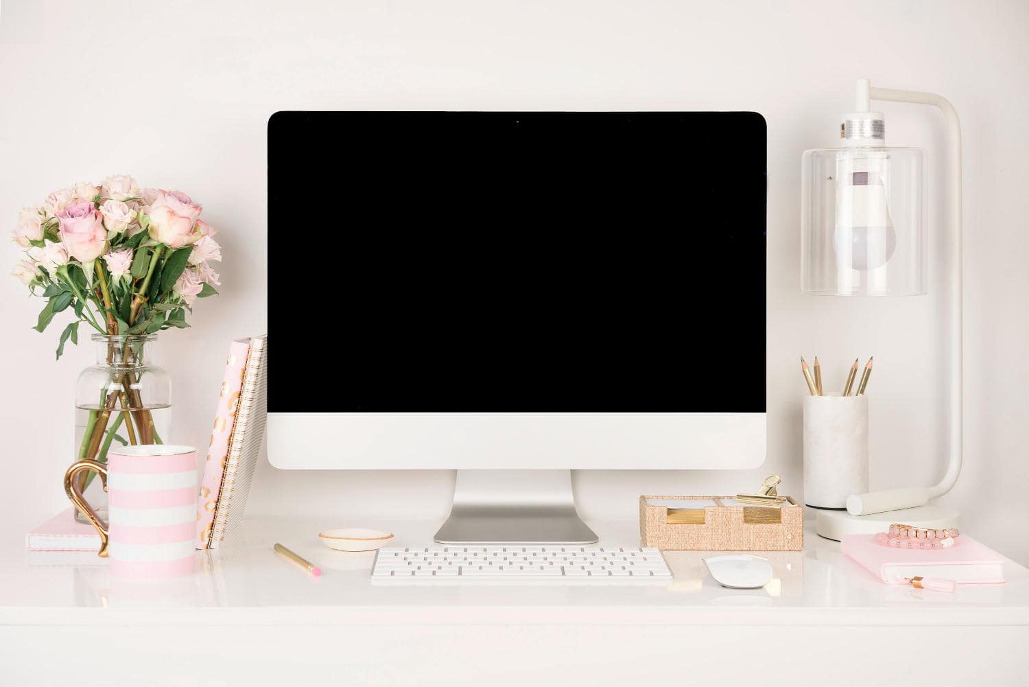 An iMac on a white desk with feminine stationery