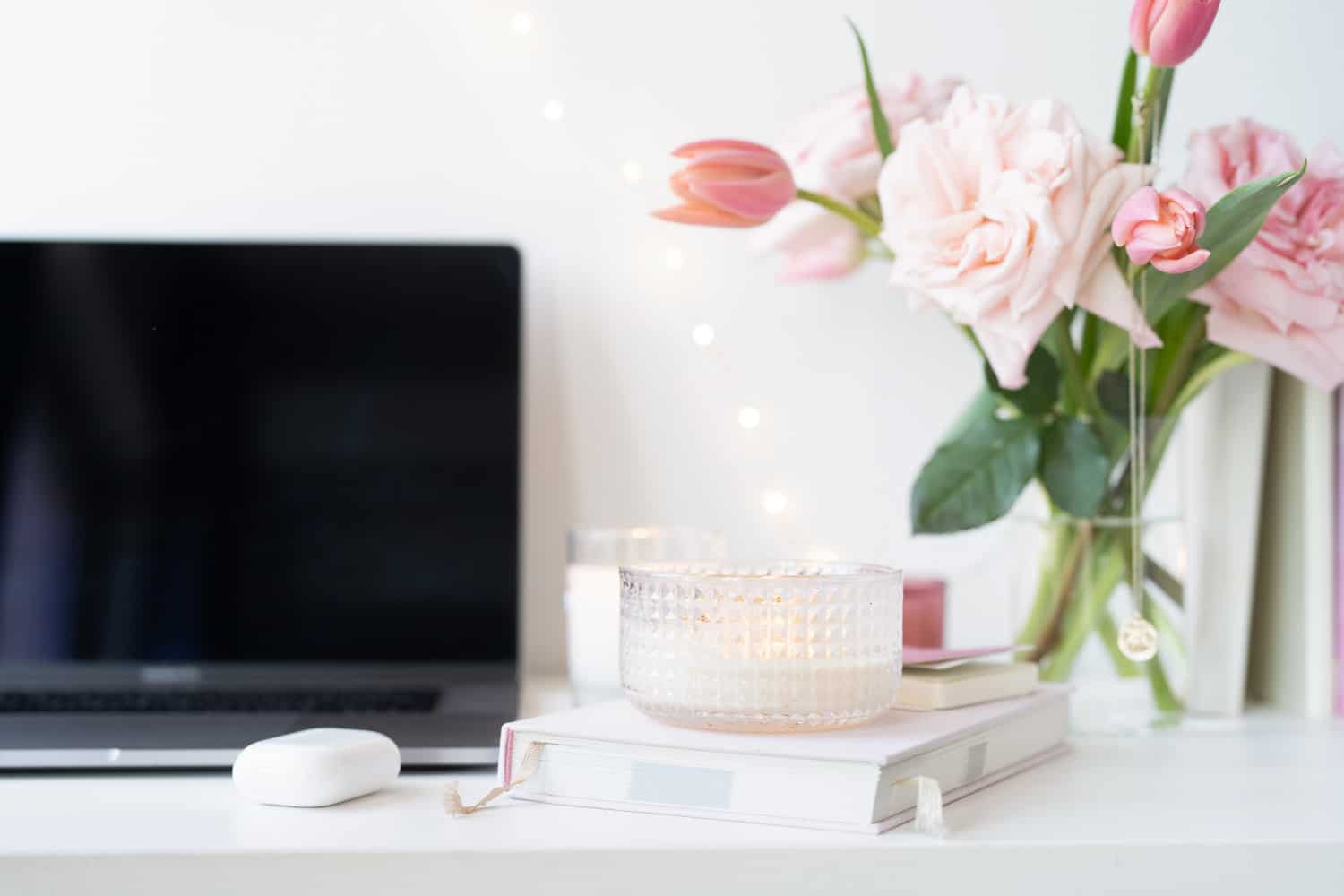 A laptop, candle, pink flowers and a notebook