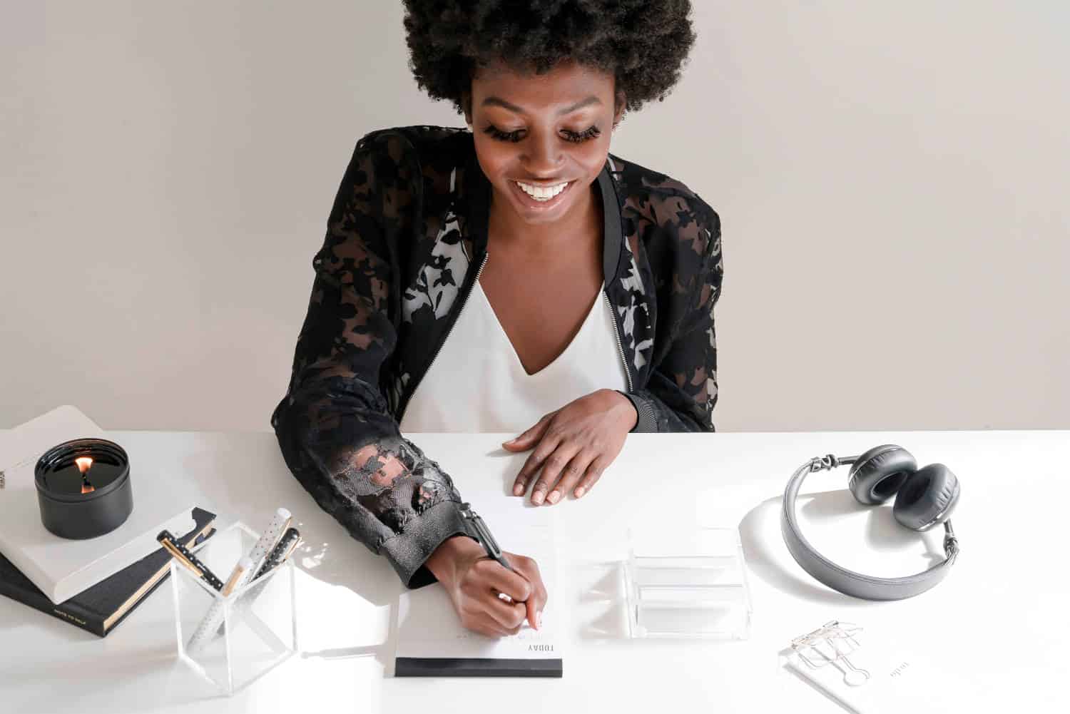 Woman writing a to-do list at a white table with headphones and white stationery