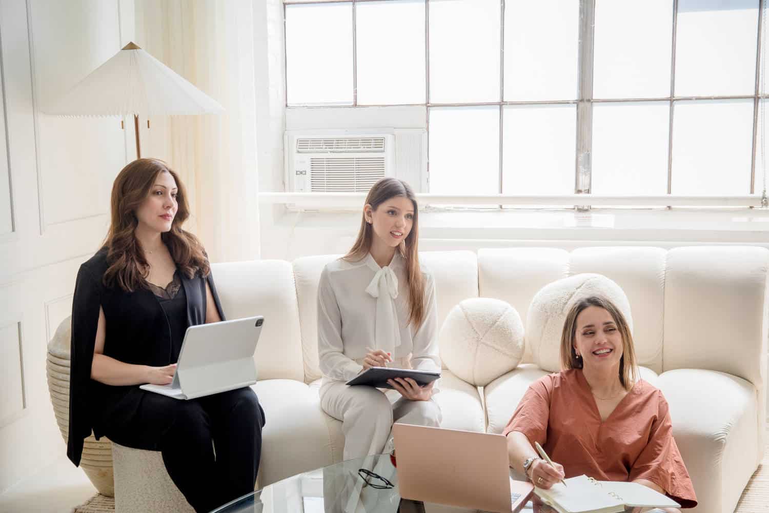 Three women sitting on a couch with laptops