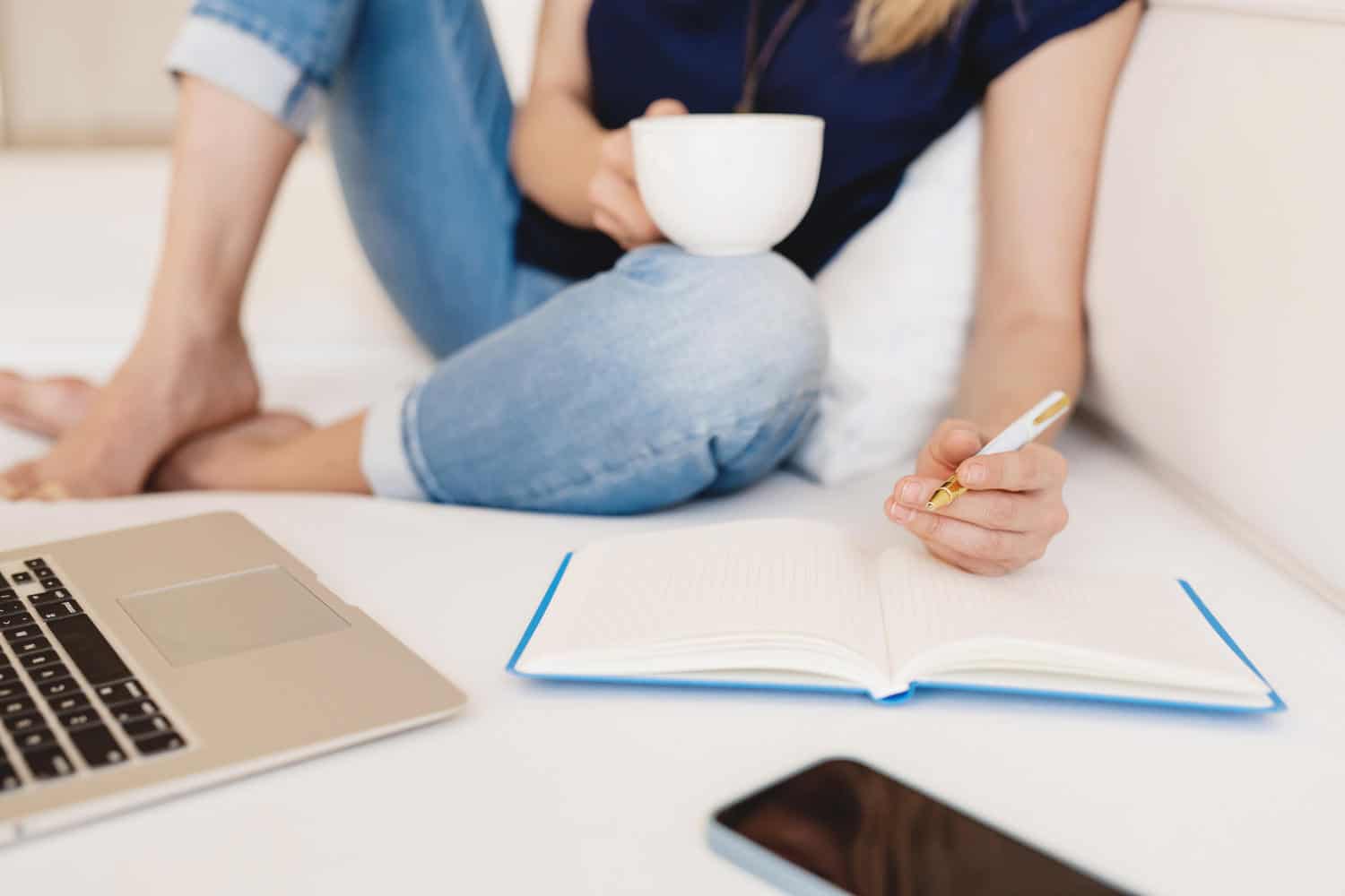 Woman sitting on the floor and writing in her blue notebook, holding a coffee cup