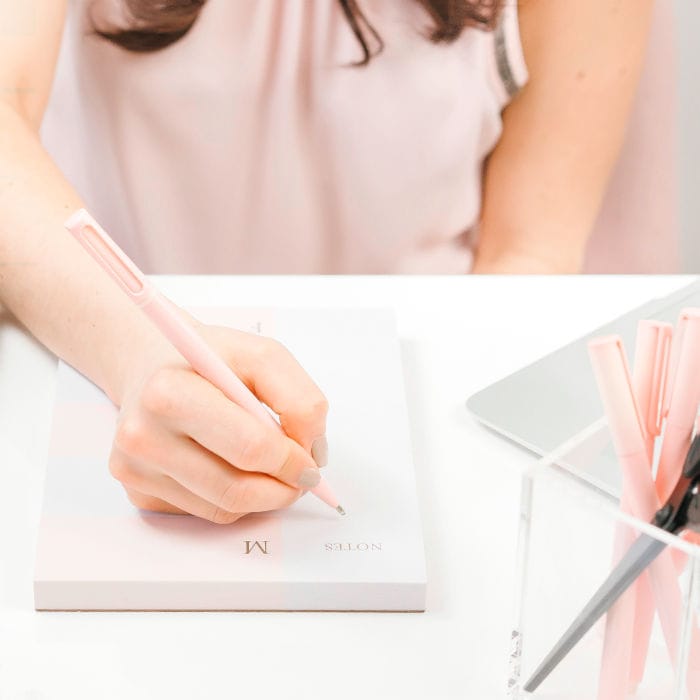 Woman sitting at a desk and writing down notes with a pink pen