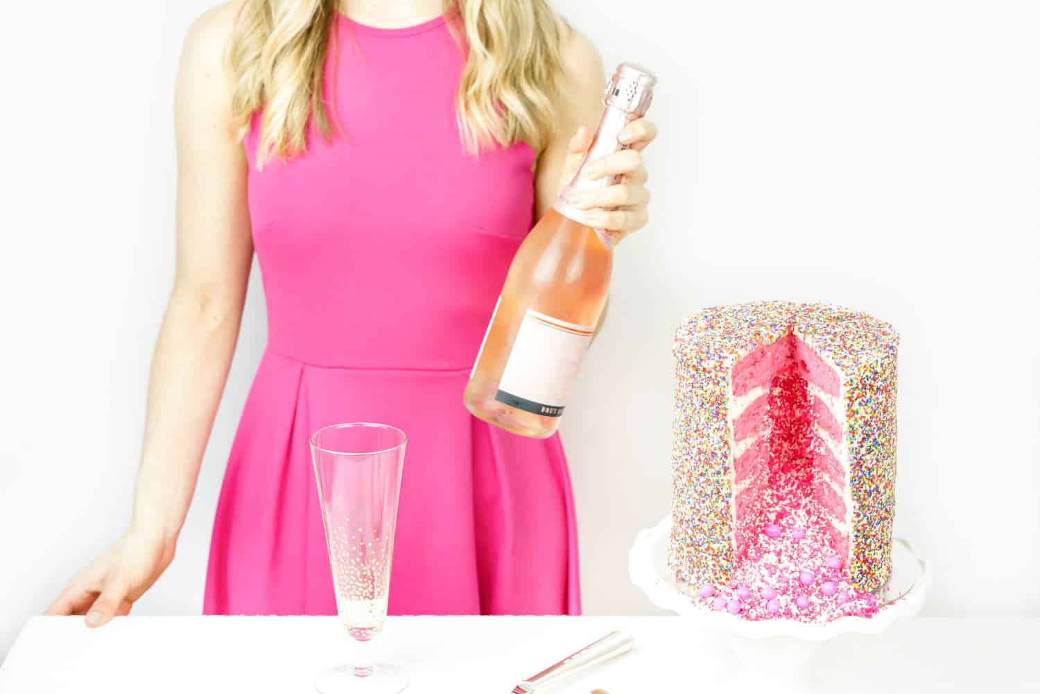 Woman in a pink dress holding a bottle next to a pink cake