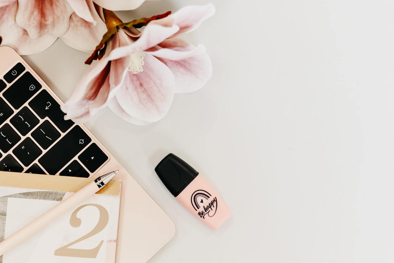 Highlighter that says be happy, a pink flower, pen and laptop