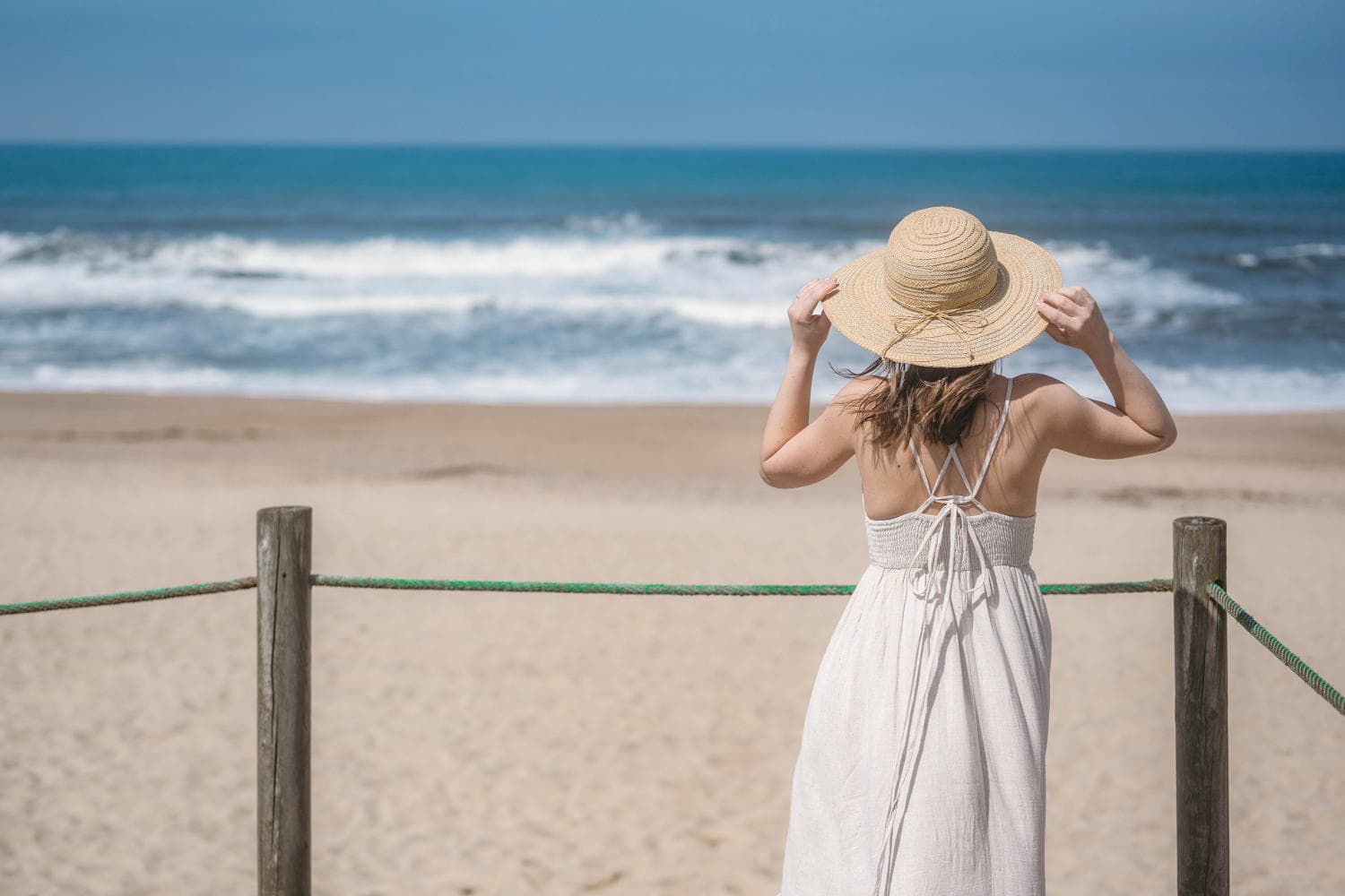 Woman looking at the ocean and holding her hat